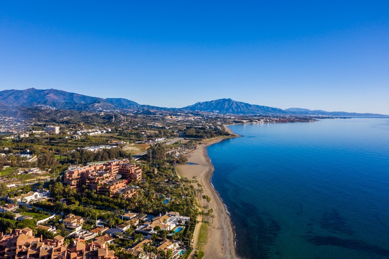 Modern luxury villa at twilight with floor-to-ceiling windows, pool reflections, and mountain views in Marbella