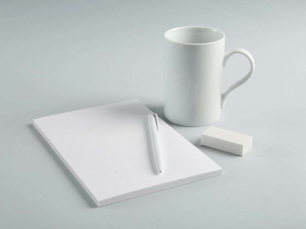 Blank mug, notepad and pen on a grey background