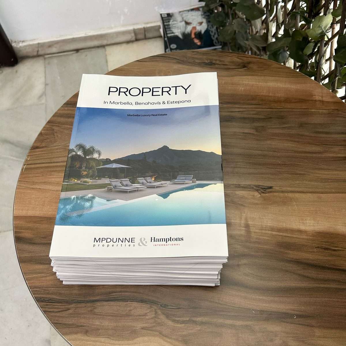 Revista inmobiliaria con portada personalizada sobre una mesa de madera en un punto de distribución de la Costa del Sol